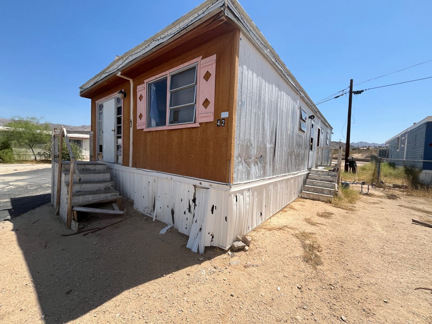 Weathered mobile home exterior with peeling skirting in the Coachella Valley desert, purchased as-is by Infinite Legacy Property Solutions